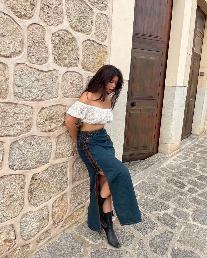 Allison wearing an off-the-shoulder white top and a lace up denim maxi skirt in a cobblestone road in Spain.